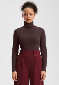 Bordowa bluzka z golfem o gładkiej fakturze, zestawiona z bordowymi, wysokim stanem spodniami ozdobionymi dwoma guzikami.