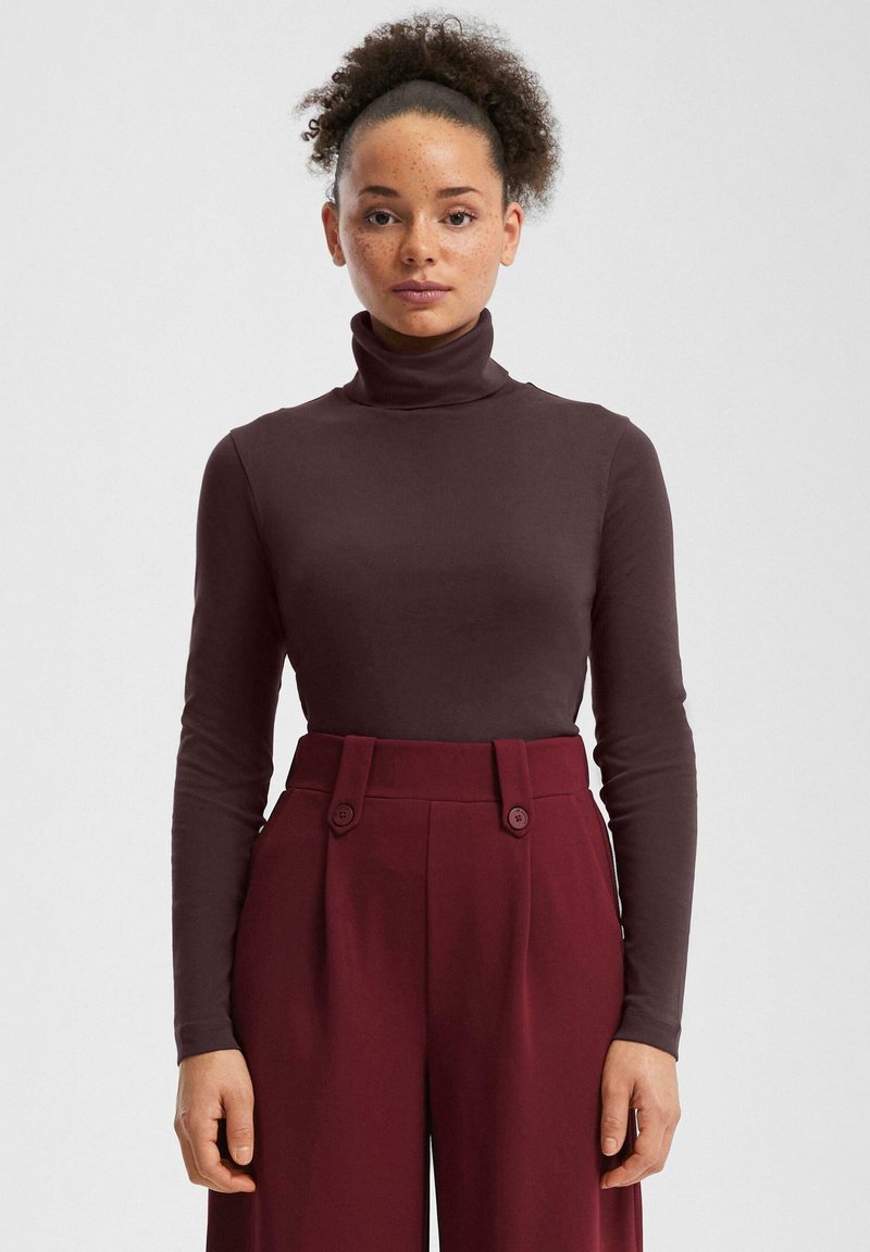 Bordowa bluzka z golfem o gładkiej fakturze, zestawiona z bordowymi, wysokim stanem spodniami ozdobionymi dwoma guzikami.
