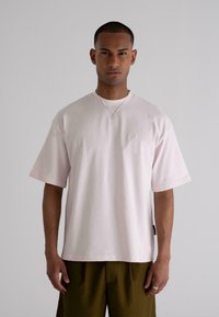 Light pink cotton t-shirt with short sleeves, round neckline, and small embroidered logo on the chest. Paired with olive green shorts.