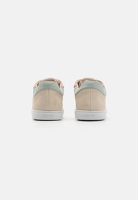 Sneakers in suede beige con accenti verde chiaro, dotati di una suola bianca liscia e una linguetta in tessuto morbido, mostrati dal retro.