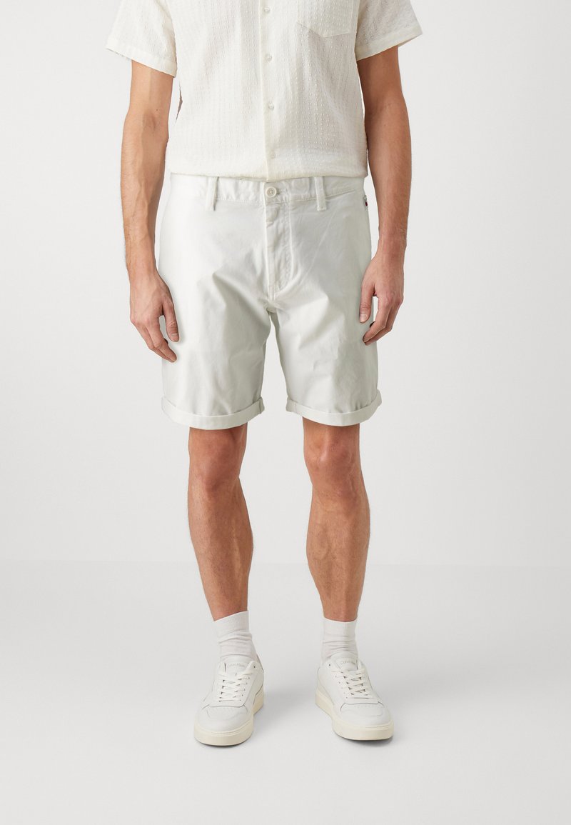 Hvite bomullsshorts med glatt overflate, oppbrett i kanten og sidelommer, kombinert med hvite joggesko og lyse sokker.