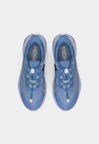 Ζευγάρι μπλε αθλητικά παπούτσια Hoka με κορδόνια γρήγορης κλειδώματος, εμφανές λογότυπο της μάρκας στο εσωτερικό και υφασμένο πάτο, από ψηλά σε λευκό φόντο.