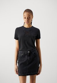 Black cotton t-shirt with short sleeves and a butterfly lace appliqué on the chest, paired with a black denim mini skirt with frayed hem.