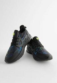 Black athletic shoes with a textured upper featuring a blue and purple splatter pattern, black laces, and a neon green accent on the tongue.