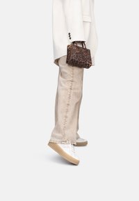 Borsa a tracolla con stampa leopardata, tenuta con manici corti, abbinata a jeans beige a gamba larga e sneakers bianche con suola beige. Elegante e moderna.