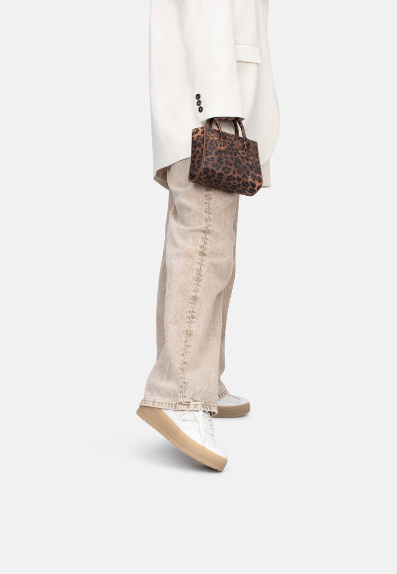 Borsa a tracolla con stampa leopardata, tenuta con manici corti, abbinata a jeans beige a gamba larga e sneakers bianche con suola beige. Elegante e moderna.