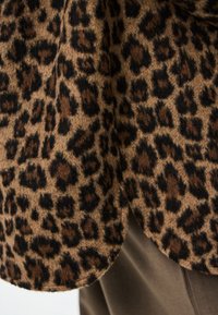 Tejido de estampado de leopardo con manchas negras y marrones sobre un fondo canela, con una textura suave. El borde tiene un dobladillo redondeado.