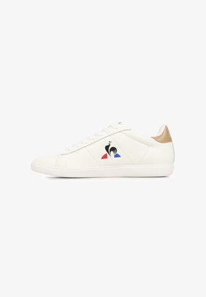 Sneaker bianca basse con linguetta beige sul tallone, logo di gallo nero sopra forme rosse e blu sul lato e lacci bianchi.