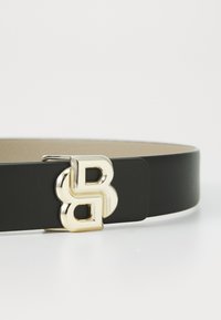 Fekete bőr öv, arany geometrikus csattal, amelyen dupla "B" dizájn található, sima felülettel és tiszta élekkel.