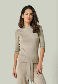 Beige gerippter Strickoberteil mit hohem Ausschnitt und Dreiviertel�ärmeln. Begleitendes gebundenes Detail an der Taille in passender Farbe.