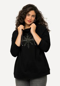 Felpa nera con cappuccio decorata con una stampa di fiocchi di neve in borchie metalliche. Tessuto morbido con una vestibilità rilassata, cordoncino e polsini a costine.