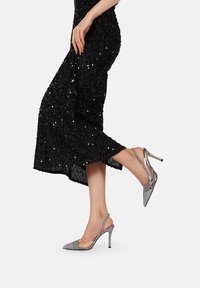 Scarpe con tacco alto grigie a slingback con punta affusolata, texture scintillante e cinturino alla caviglia, che si abbinano a una gonna nera di paillettes.