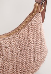 Gros plan d’un sac à main tissé beige avec une fermeture éclair dorée et une lanière marron clair sur un fond uni.