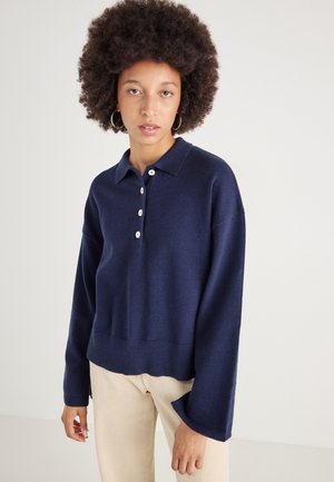 Pull-over bleu marine avec col, patte de boutonnage à quatre boutons, épaules tombantes et ourlet côtelé. Texture douce et coupe décontractée.
