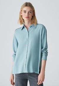 Lichtblauw button-up shirt met lange mouwen, voorzien van een kraag en zijsplitten. Gemaakt van een zachte, lichte stof.
