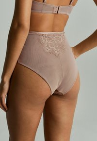 Hochgeschnittene Unterwäsche aus weichem nude-farbenem Netz mit einem dekorativen Spitzeneinsatz auf der Rückseite. Verfügt über eine glatte Textur und subtile Designelemente.