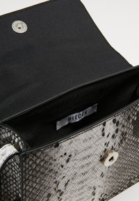 Černá kabelka s hadím vzorem, texturovaným povrchem, stříbrným zacvakávacím uzávěrem a látkovou podšívkou. Štítek uvnitř nese nápis "PIECES".