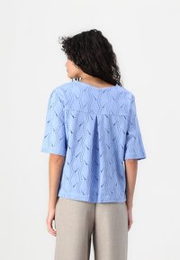 Lichtblauw T-shirt met korte mouwen en een golfpatroon, met een ronde halslijn en geplisseerd detail aan de achterkant. Zachte, ademende stof.