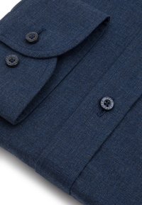 Ciemnoniebieska koszula z teksturowanej tkaniny. Posiada zapięcie na guziki, dwa czarne guziki oraz złożony kołnierzyk z ostro zakończonymi krawędziami.