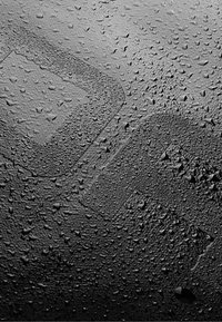 Čierny textúrovaný povrch pokrytý kvapkami vody, so slabým obrysom obdĺžnikového tvaru v ľavom hornom rohu.