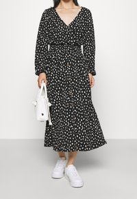 Musta mekko, jossa valkoisia pilkkuja, v-pääntie, pitkähihaiset, napillinen edestä ja vyötärö kavennettu. Yhdistetty valkoisiin tennareihin ja pieneen laukkuun.