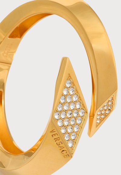 Βραχιόλι Versace σε χρυσό χρώμα με μυτερά άκρα διακοσμημένα με καθαρά κρύσταλλα σε σχήμα διαμαντιού σε κάθε άκρο, γυαλιστερό φινίρισμα.