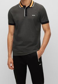 Polo shirt nera a maniche corte con motivo a pois, colletto arancione e bianco a contrasto, patta con tre bottoni e logo ricamato "BOSS".