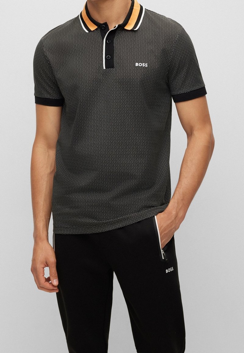 Polo shirt nera a maniche corte con motivo a pois, colletto arancione e bianco a contrasto, patta con tre bottoni e logo ricamato "BOSS".