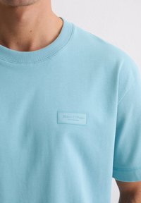 Jasnoniebieska bawełniana koszulka z prążkowanym okrągłym dekoltem i naszywką z napisem "Marc O'Polo." Gładka faktura, casualowy, luźny krój.