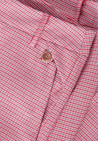 Tissu à carreaux rouge et blanc avec un motif texturé, présentant un bouton marron et des coutures sur mesure. Vue rapprochée des détails de design.