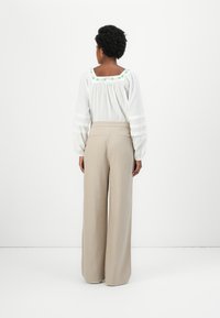 Blusa branca com decote bordado em verde e mangas listradas transparentes, combinada com calças largas beijas com bolsos traseiros.