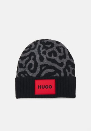 Beanie en tricot noir avec un motif abstrait gris, terminé par une bordure côtelée. Une étiquette rouge porte le texte "HUGO" en noir.