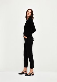 Suéter negro de canalé, jeans negros de cintura alta y zapatos de tacón bajo tipo slingback en negro, todos con un diseño elegante y minimalista.