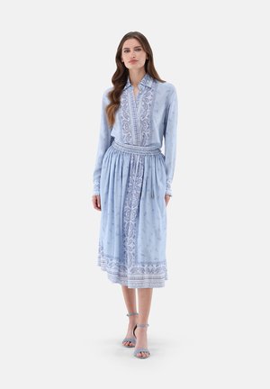 Helles blaues Kleid mit langen Ärmeln, Kragen-Design und Paisley-Muster-Akzenten. Der Rock ist an der Taille gerafft und fließt bis zur Mitte der Wade.