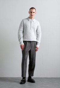 Grå strikket polo sweater med krave, parret med grå plisserede bukser og sorte loafers. Glatte teksturer og skræddersyet pasform.