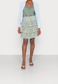 Hellblau bomberjacke über einem grünen camisole, kombiniert mit einem gestuften mini-rock mit einem grün-weißen blumenmuster und mintfarbenen sandalen.