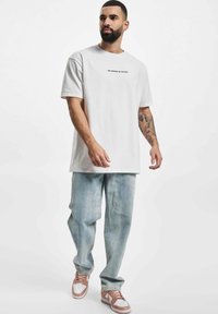 Hvid bomulds t-shirt med "VI DREMMER I FARVER" trykt i sort, parret med lyseblå denim jeans og brune sneakers.