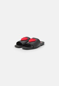Black slide sandals with open toe, featuring red crocheted heart accents on the straps and a smooth, flat sole.