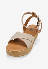 Sandalias de plataforma beige con tiras cruzadas de material suave, con una plantilla en tono bronceado y una suela parecida al corcho, correa ajustable en el tobillo con hebilla plateada.
