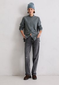 Checked shirt in navy and green with button closure, paired with distressed grey jeans and brown shoes, set against a plain background.