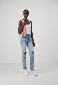 Top bianco, jeans strappati azzurri chiaro, borsa lavorata a maglia (arancio, rosa, bianco) e sneakers bianche con dettagli pastello. Sono presenti occhiali da sole.