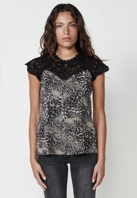 Top con stampa leopardata e maniche a cappuccio in pizzo nero all'uncinetto. Tessuto seta, design a scollo a V. La modella lo indossa con jeans scuri.