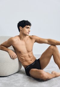 Crne pamučne bokserice s Calvin Klein logotipom na pojasu, prikazane na muškom modelu protiv neutralne pozadine.