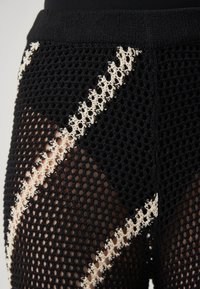 Leggings en mesh noirs avec un motif orné d'accents crème et une taille texturée. Le matériau est léger avec des sections en maille ouverte.