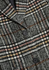 Blazer doppiopetto in un tessuto a quadri testurizzato nero, bianco e arancione, dotato di rever a punta e due bottoni neri.