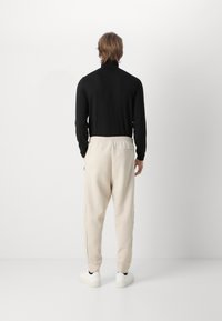 Sort langærmet skjorte og beige sweatpants med elastisk talje, sidelommer og ribbede manchetter; båret med hvide sneakers.
