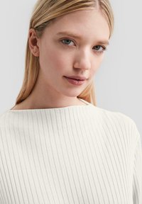 Biały prążkowany top dzianinowy z szerokim dekoltem, gładką fakturą i dopasowanym krojem, ozdobiony delikatnymi, subtelnymi pionowymi liniami.