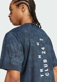 Camiseta de color azul marino con un patrón texturizado, con el texto vertical en blanco "TRAINING CLUB 24/7" en la parte posterior. Mangas cortas.
