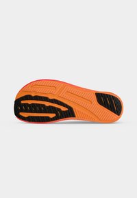 Semelle de chaussure avec une base orange et des sections de grip en caoutchouc noir, présentant des motifs texturés pour la traction et le soutien.