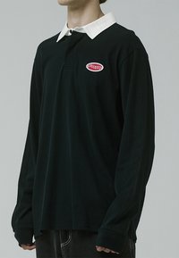 Black long-sleeve polo with a white collar, featuring a red embroidered logo on the chest. Soft fabric, relaxed fit. Minimalist design.